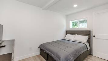 Quarto com cama, janela, porta e escrivaninha com controle remoto.