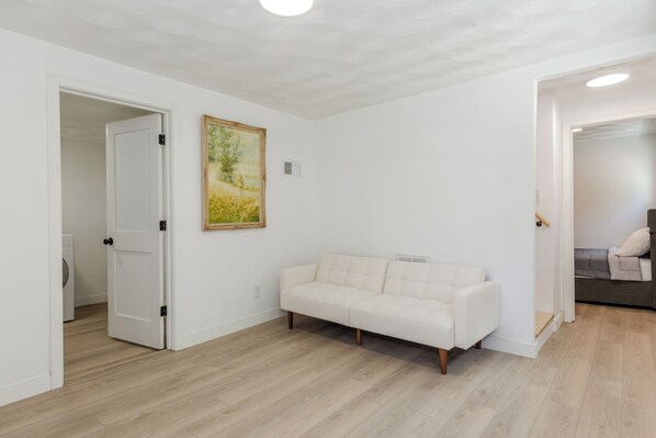 A room with a white sofa, a painting on the wall, and a door leading to another room.