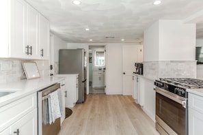 A modern kitchen with white cabinetry, a stainless steel refrigerator, a gas stove, and a tiled backsplash.