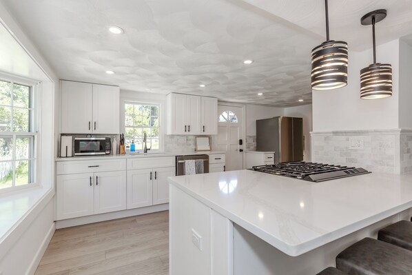 A modern kitchen with white cabinetry, a central island, stainless steel appliances, and pendant lighting.
