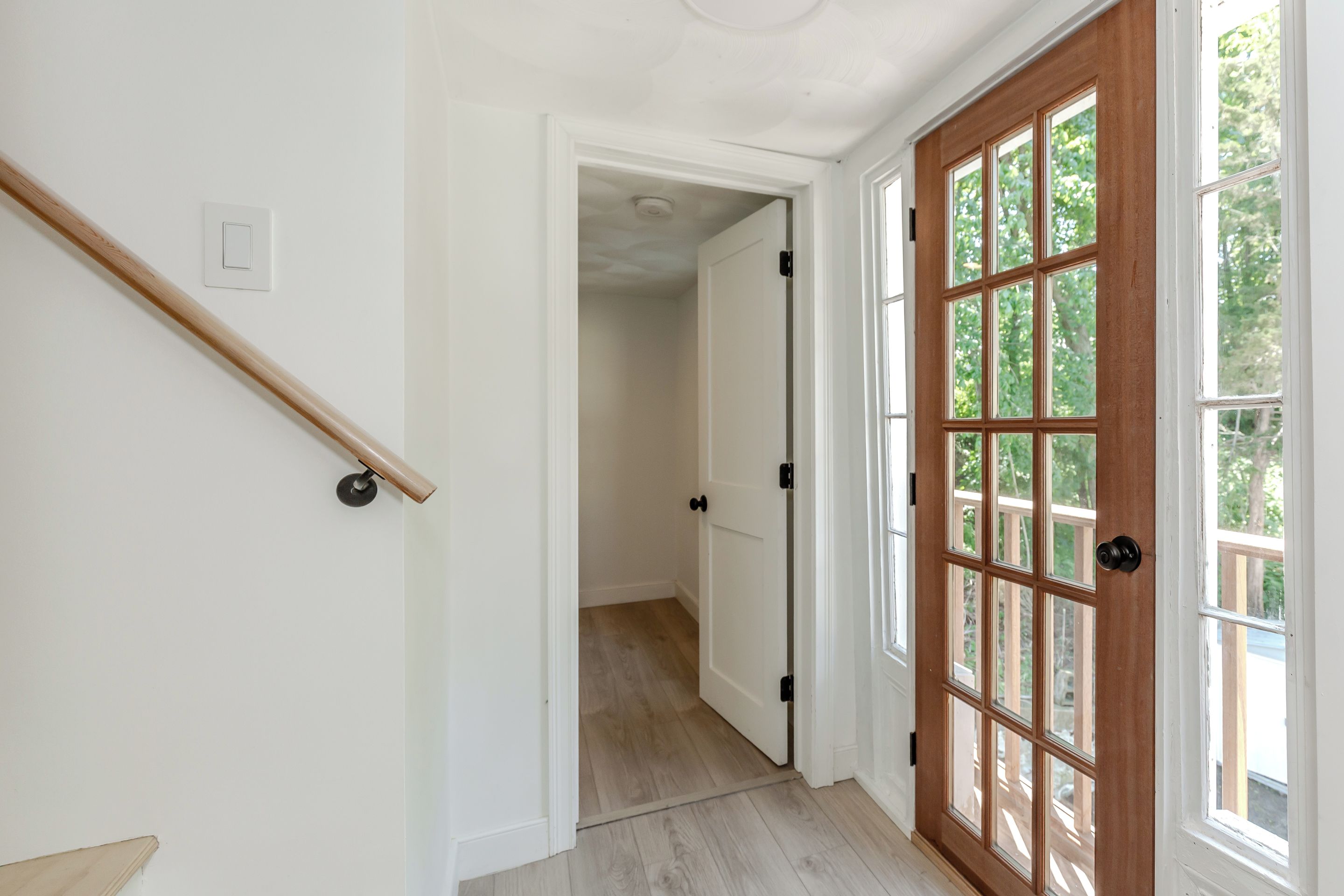 Un couloir avec une rambarde en bois, des murs blancs et une porte en bois dotée de panneaux de verre.