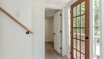 Un couloir avec une rambarde en bois, des murs blancs et une porte en bois dotée de panneaux de verre.