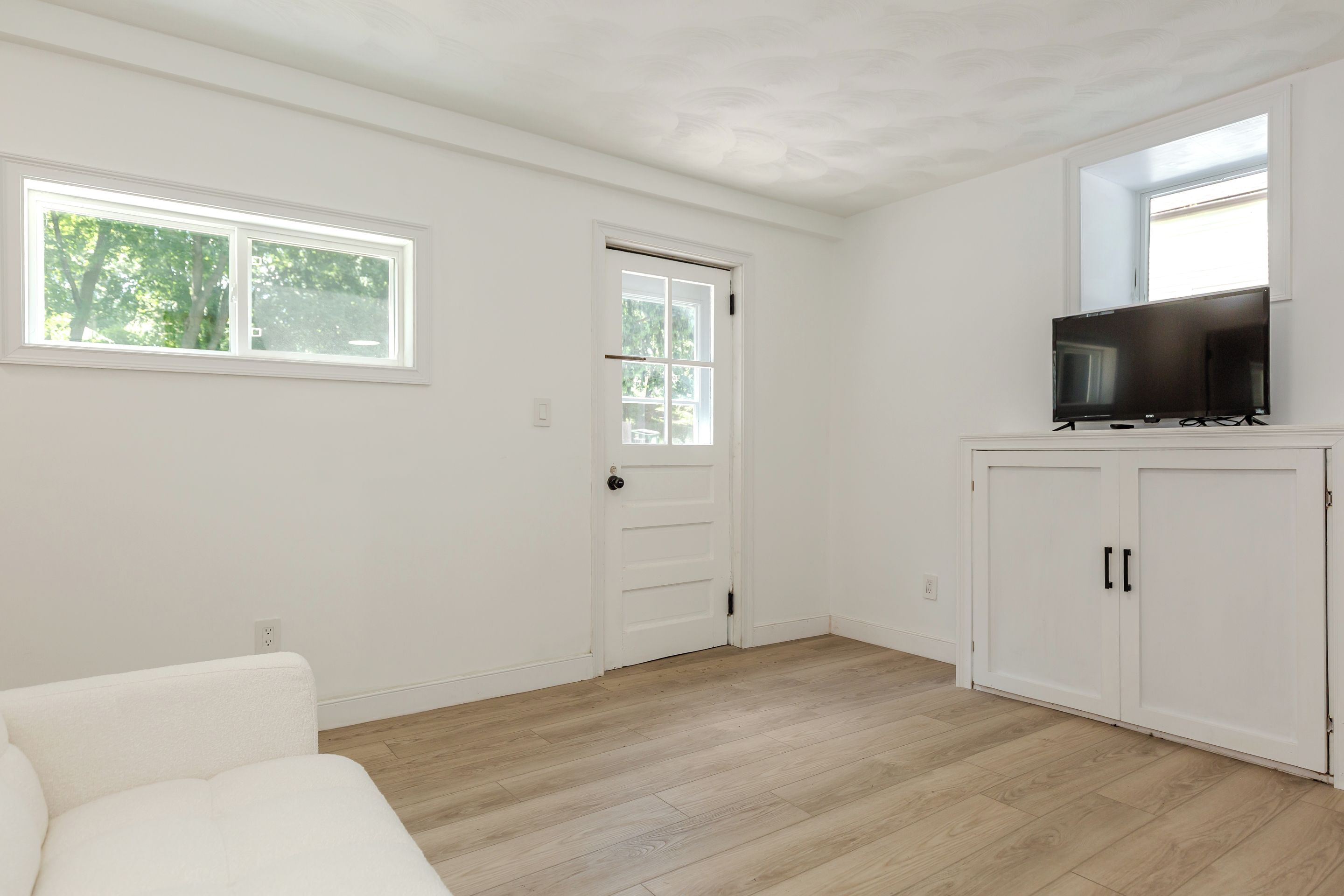 A room with a white door, a television on a stand, and a window with a view of trees.