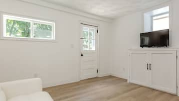 A room with a white door, a television on a stand, and a window with a view of trees.