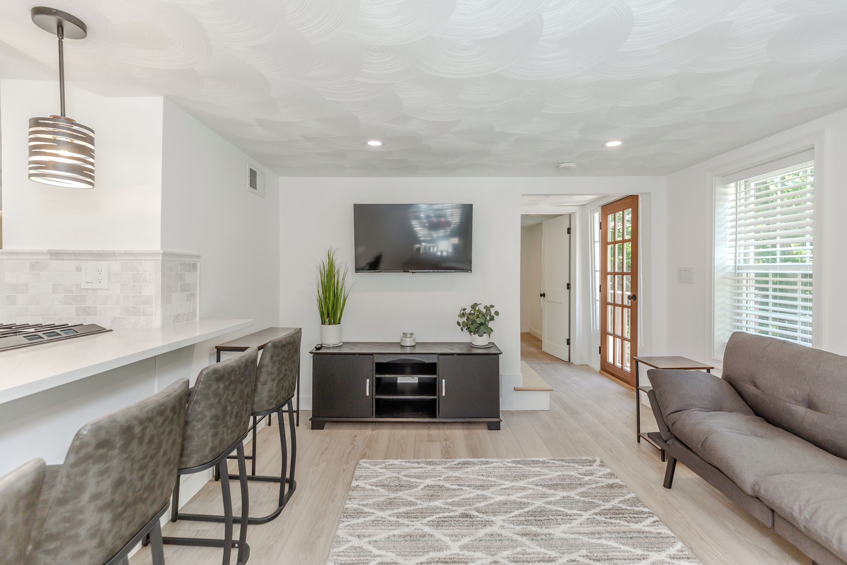 Sala de estar moderna com sofá cinza, área de jantar com balcão e TV fixada na parede.