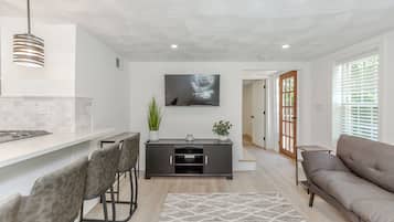 Sala de estar moderna com sofá cinza, área de jantar com balcão e TV fixada na parede.