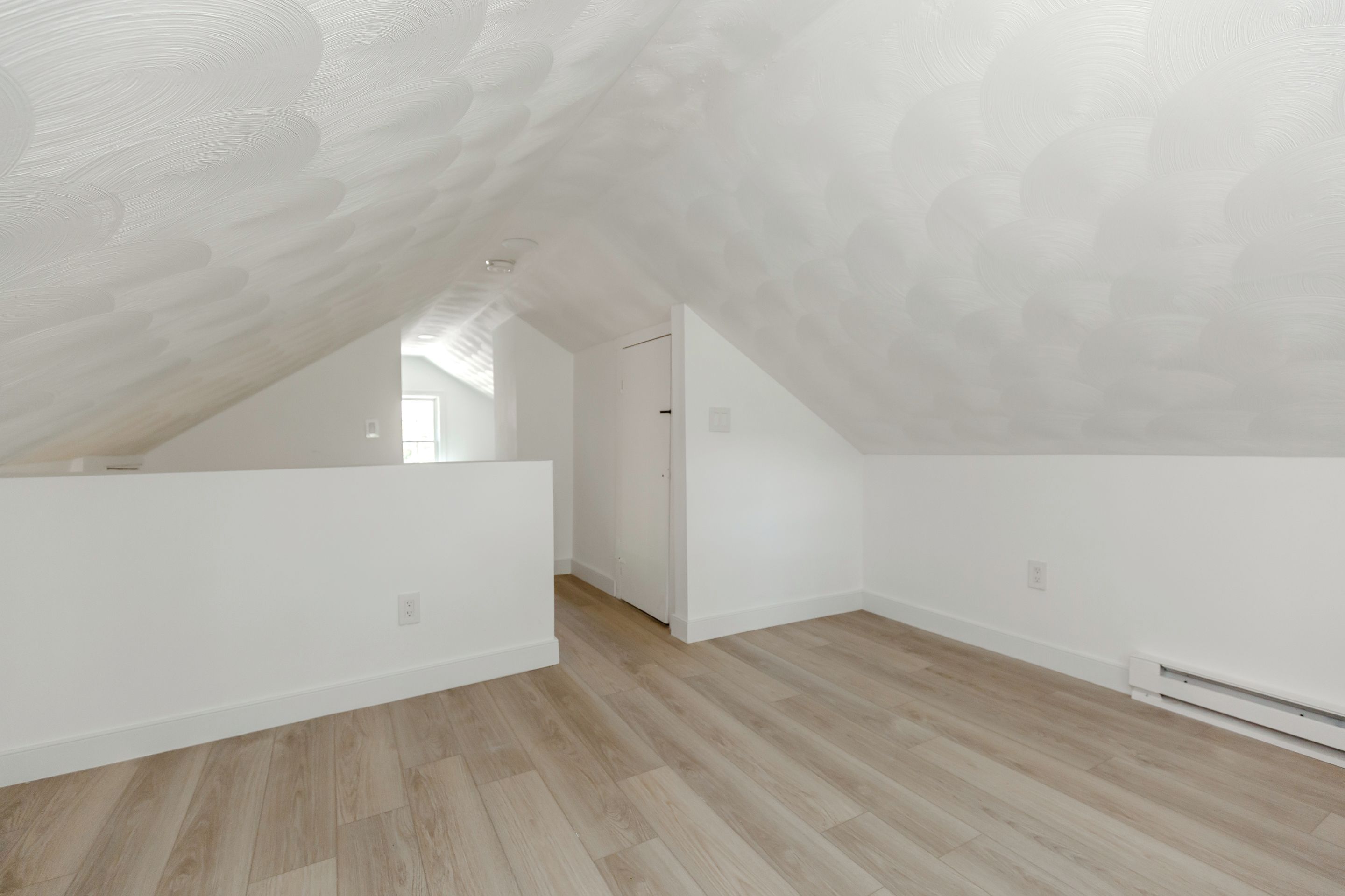 Um quarto de sótão espaçoso com piso de madeira, paredes brancas e teto inclinado.