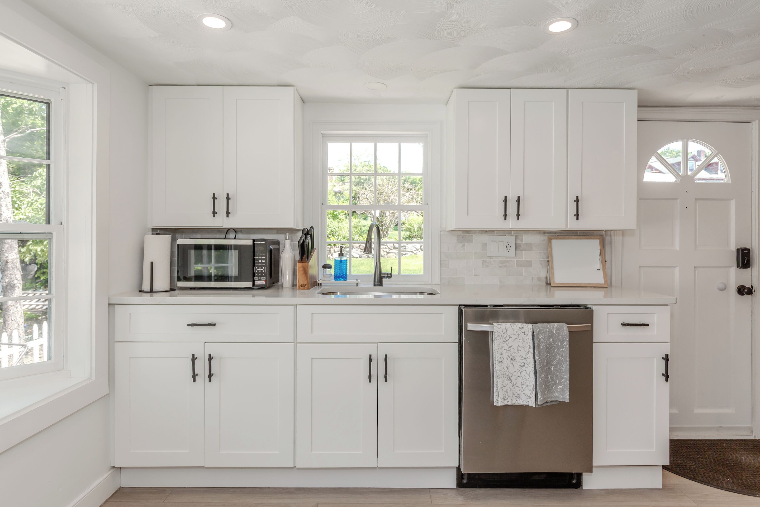 Una cocina moderna con armarios blancos, un refrigerador de acero inoxidable y un microondas.