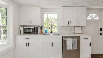 Una cocina moderna con armarios blancos, un refrigerador de acero inoxidable y un microondas.