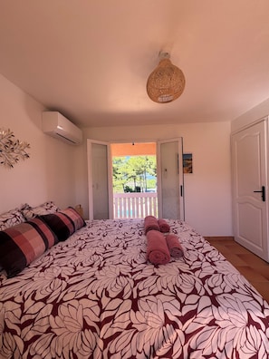 A bedroom with a bed, an air conditioning unit, a hanging light fixture, and a view of an outdoor balcony. - Villa Souleou - Giens Peninsula - Swimming Pool (Hyères)
