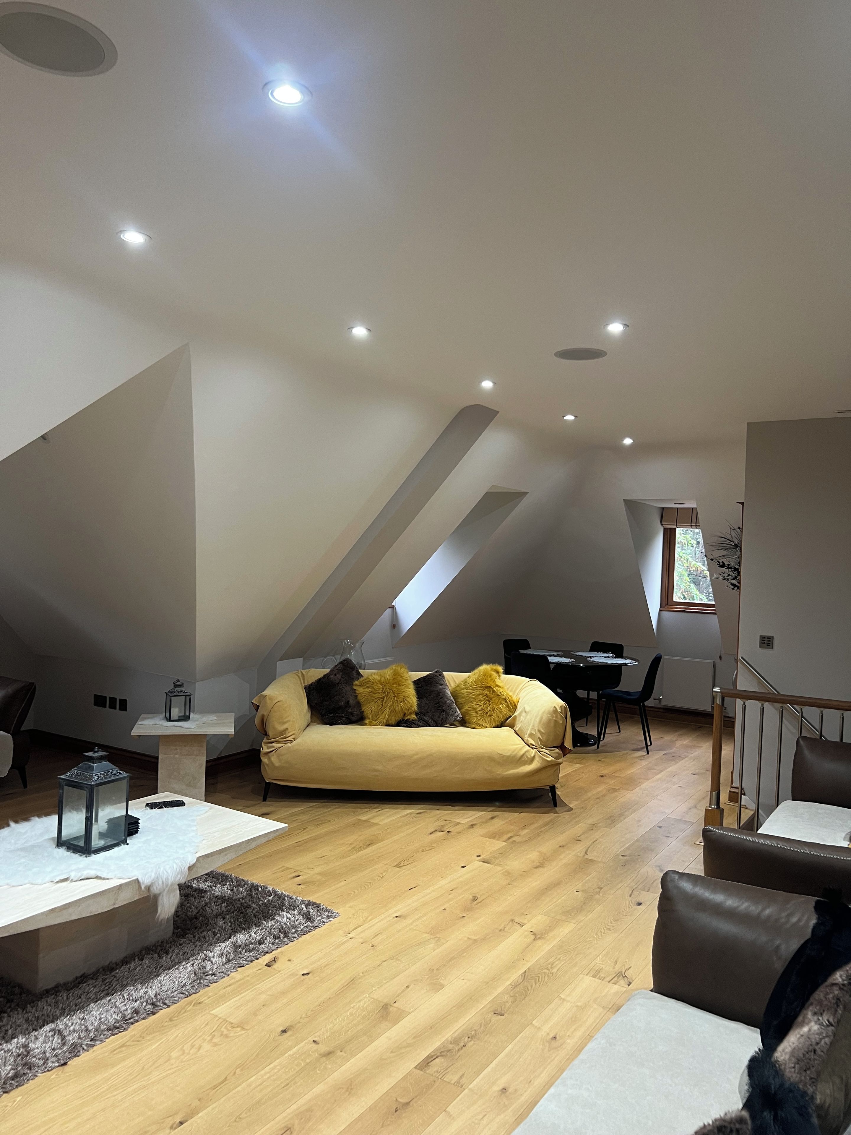 A modern loft with a high ceiling, a sofa with cushions, a dining table, and a staircase.