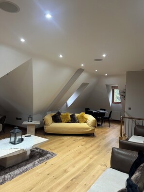 A modern loft with a high ceiling, a sofa with cushions, a dining table, and a staircase. - My place of peace (Henfield)