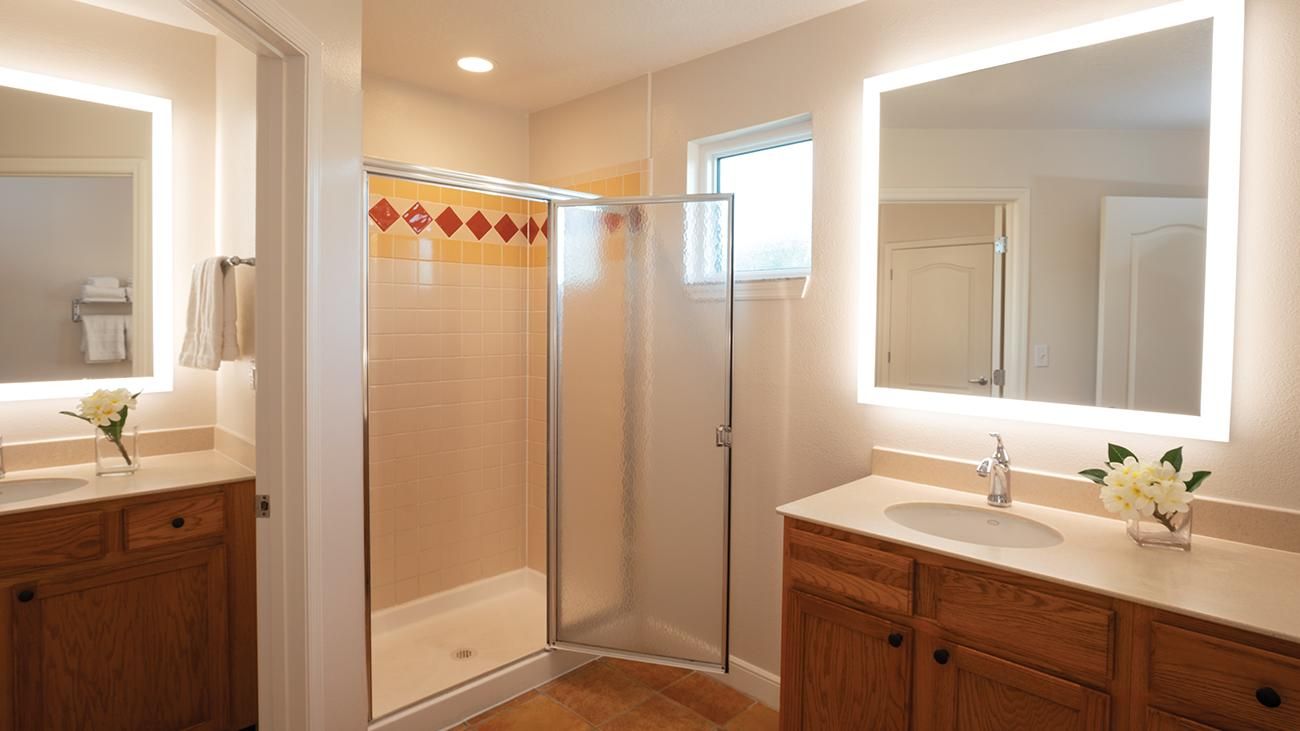 A bathroom with a glass shower enclosure, wooden cabinets, and a large mirror above the sink.