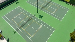 Een tennisbaan met meerdere velden, netpalen en omliggend hekwerk.