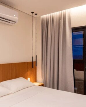 A hotel room with a bed, an air conditioning unit, a bedside table with a lamp, and a window with curtains. - Apartment in Salinas, Premium Hotel Resort (Salinópolis)