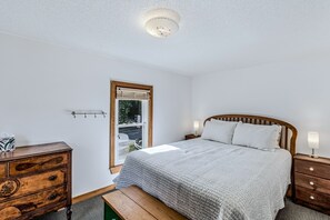 Ein Schlafzimmer mit einem Bett, Nachttischen, einer Holzkommode, einer Bank und einer Deckenleuchte.
