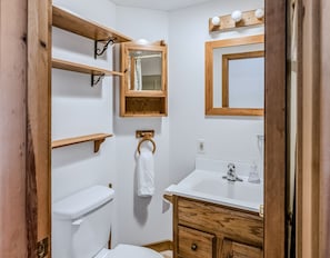Een badkamer met toilet, wastafel, houten planken, een handdoekhouder en een spiegel.