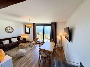 A modern living room with a sofa, dining table, chairs, and a large window with a mountain view. - 250m from ski lifts, 3rd floor, balcony, tv, 41m², Alpe d'Huez (L'Alpe d'Huez)