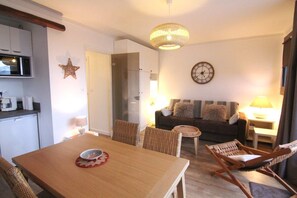 A dining area with a wooden table, wicker chairs, a small round table with a lamp, a sofa with cushions, and a wall clock. - 250m from ski lifts, 3rd floor, balcony, tv, 41m², Alpe d'Huez (L'Alpe d'Huez)