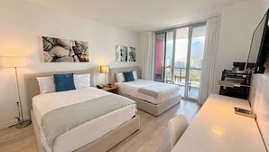 Quarto de hotel com duas camas, uma escrivaninha, uma televisão e varanda com vista para a cidade.