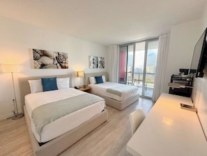 Une chambre d’hôtel avec deux lits, un bureau, une télévision et un balcon donnant sur la ville.