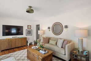 A living room with a sofa, coffee table, and a television. There is a cabinet and a mirror on the wall. - The Sivley House (Oxford)