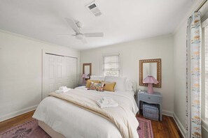 Quarto com cama, mesas de cabeceira, ventilador de teto, janela com persianas e uma porta.