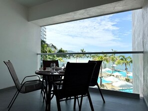 Ein Balkon mit Tisch und Stühlen, mit Blick auf einen Pool und Palmen.