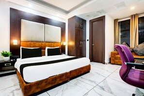 A modern bedroom with a large bed, dark wooden wardrobe, and a seating area with a purple chair. - Super Townhouse Sector 52 (Gurugram)