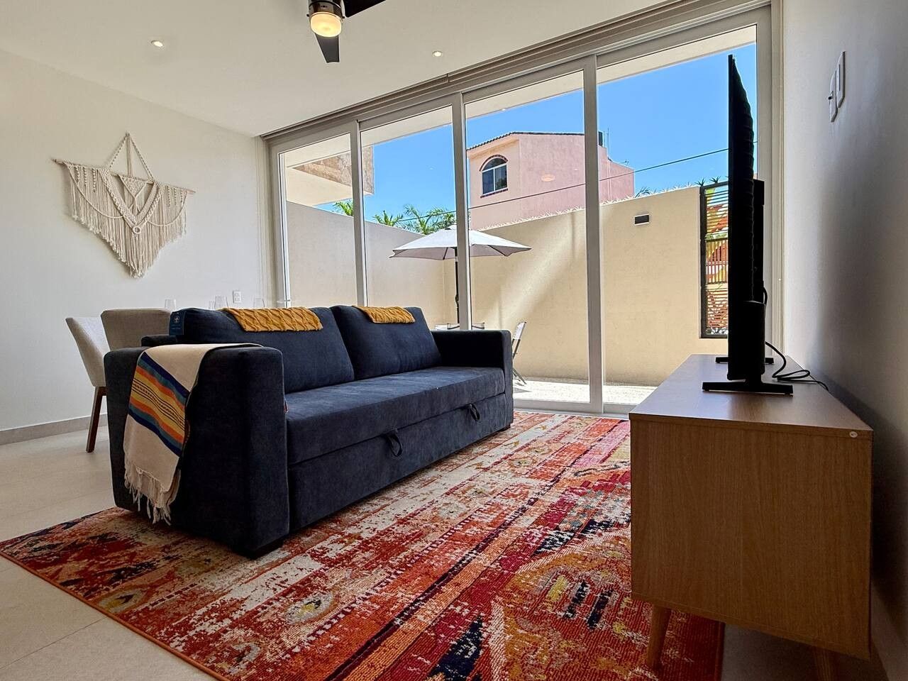 Una sala de estar con un sofá, un televisor sobre un mueble bajo y un ventanal con vistas a edificios.
