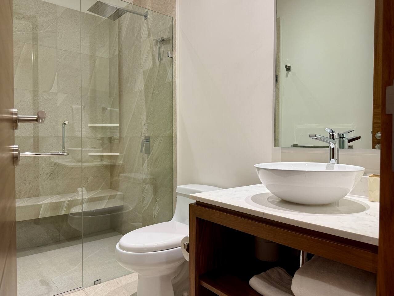 A bathroom with a glass-enclosed shower, a white toilet, and a large white sink with a wooden vanity.