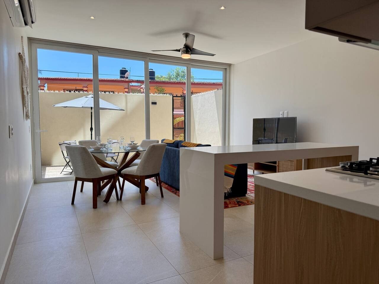 A modern kitchen with a dining area, large windows, and a ceiling fan.