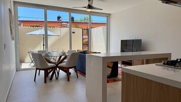 A modern kitchen with a dining area, large windows, and a ceiling fan.