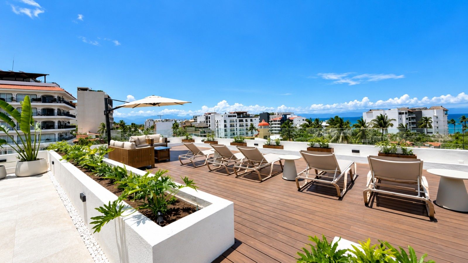 A rooftop terrace with lounge chairs, planters, and a view of the ocean and buildings.