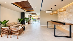 A modern lobby with a sofa, chairs, a coffee table, a long table, and hanging lights.