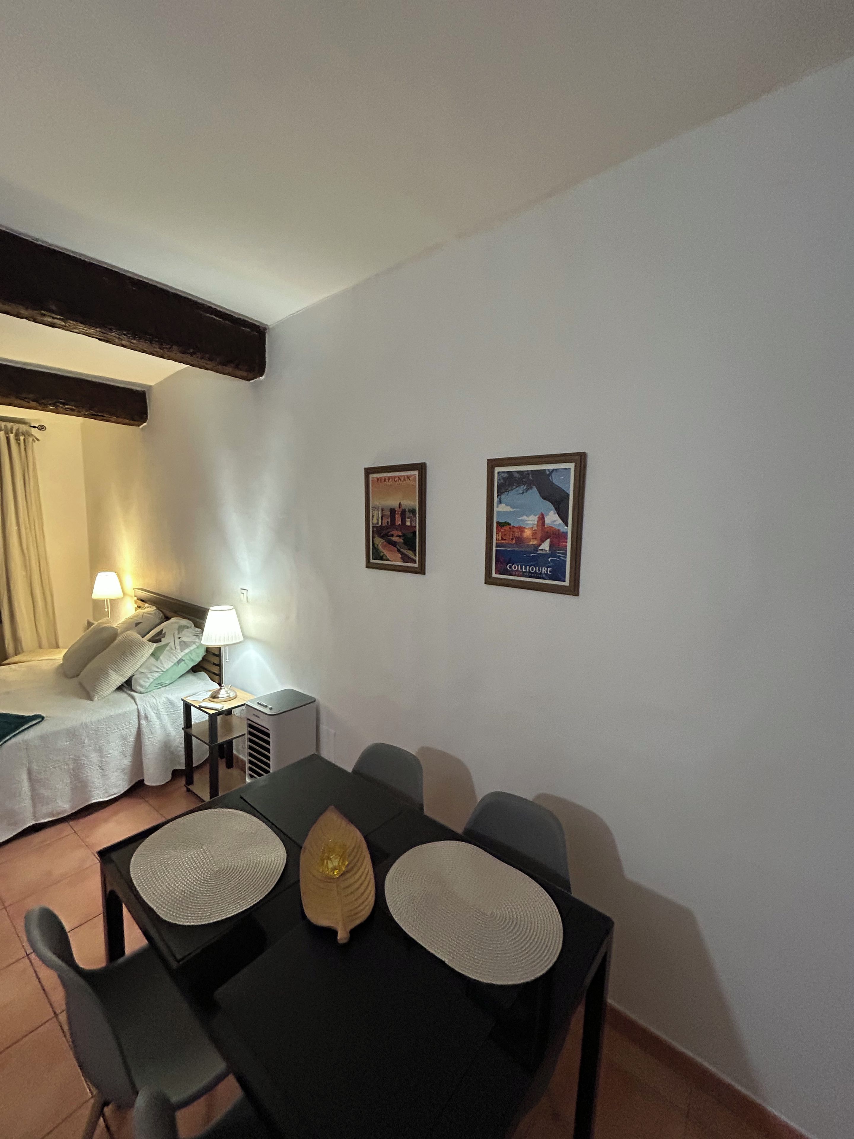 A hotel room with a bed, bedside lamps, a table with chairs, and two framed pictures on the wall.