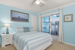 A bedroom with a bed, a nightstand, a lamp, a framed picture, and a sliding glass door leading to another room. - A Beach Escape | Ocean Balcony, Bunk Room, Dogs OK (North Topsail Beach)