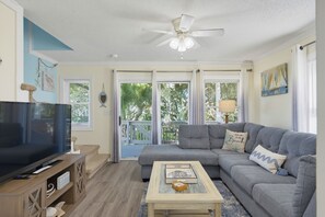 A living room with a grey sofa, a coffee table, a television, and a ceiling fan. - A Beach Escape | Ocean Balcony, Bunk Room, Dogs OK (North Topsail Beach)