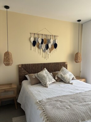 Ein Schlafzimmer mit einem Bett, zwei Nachttischen, einem Wandbehang aus Makramee und zwei Pendelleuchten.