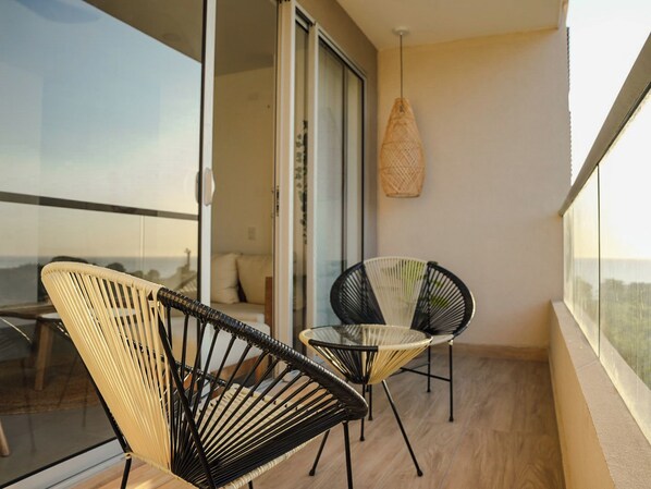 Ein Balkon mit zwei Stühlen, einem Glastisch und einer hängenden Leuchte.