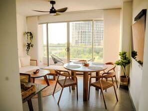 A modern living room with a round dining table, wicker chairs, a sofa, and a large window with a city view. - Santa Marina Sierra & Caribbean Retreat (Santa Marta)