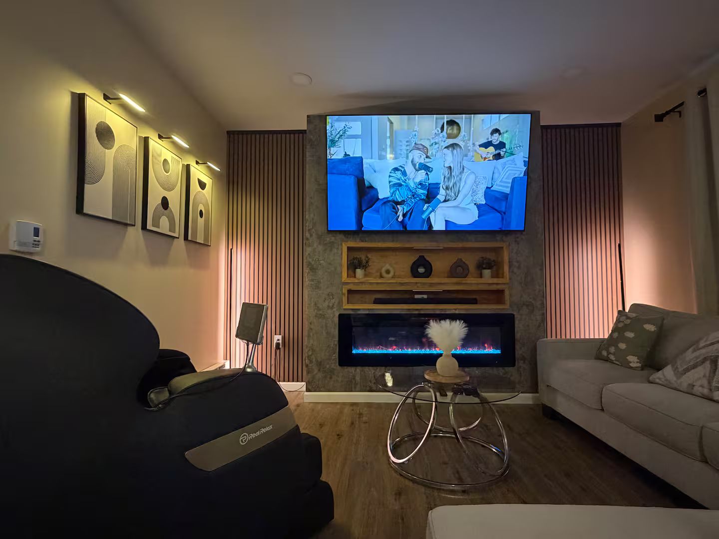 A living room with a flat-screen TV, a massage chair, a sofa, and a fireplace.