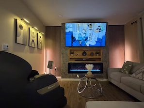 Ein Wohnzimmer mit Flachbildfernseher, Massagesessel, Sofa und Kamin.