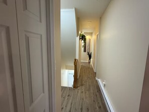 A hallway with a wooden floor, white walls, and a door on the left.