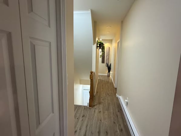 A hallway with a wooden floor, white walls, and a door on the left.