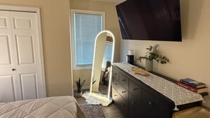A bedroom with a bed, a dresser, a mirror, a window with blinds, a wall-mounted TV, and a small plant. - Spacious Luxury 3BR by Lake & Park in Roselle (Roselle)