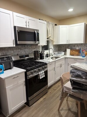 A modern kitchen with white cabinets, a stainless steel stove, a microwave, and a sink.