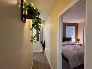 Ein Flur mit Holzboden, der zu einem Schlafzimmer mit Bett und Fenster führt.