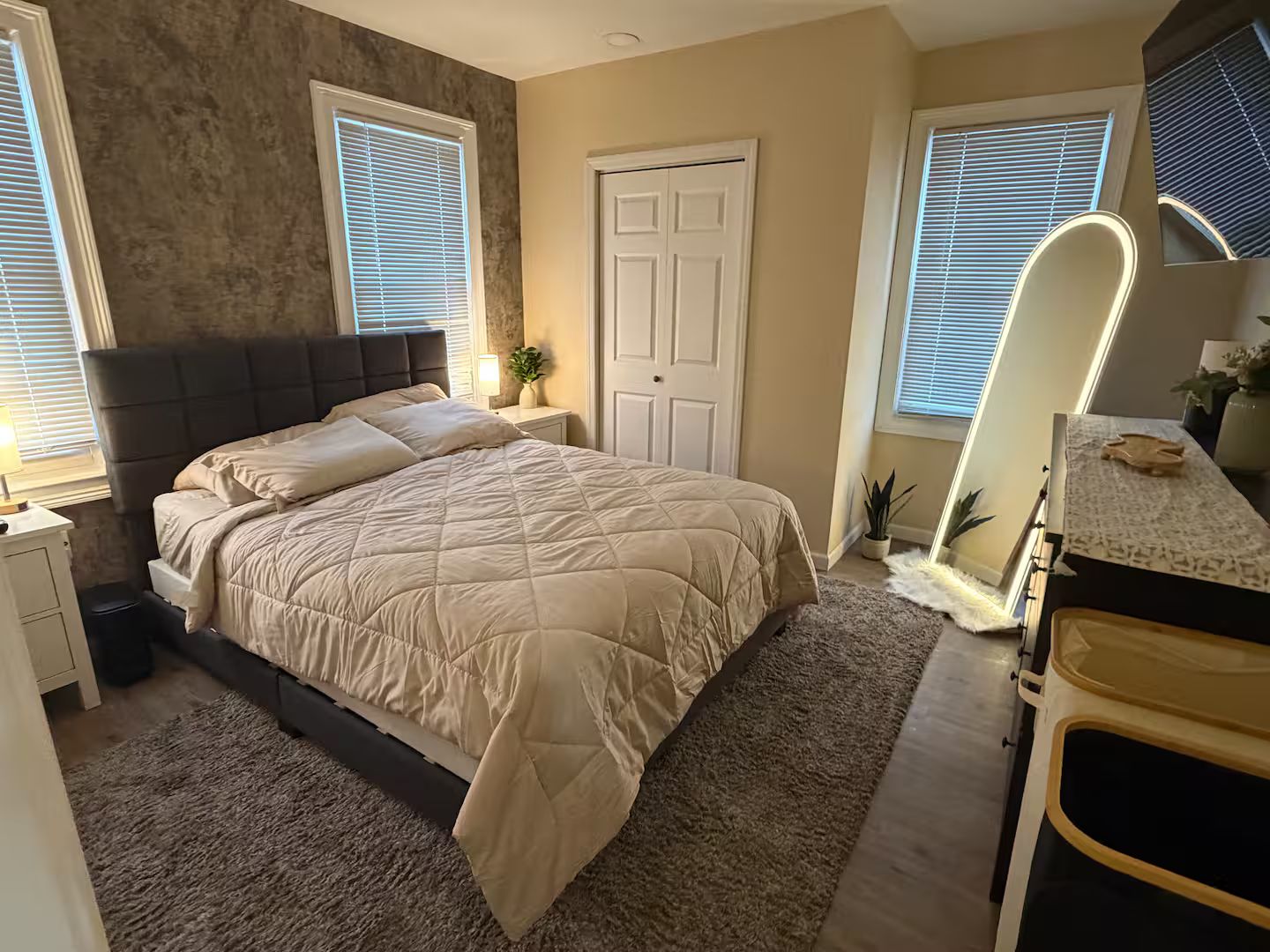 A bedroom with a bed, bedside tables, a dresser, a mirror, and a door.