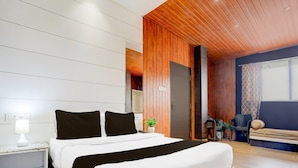 A modern bedroom with a large bed, a nightstand, a bedside lamp, a wooden ceiling, and a view of the outside. - Collection O Jaigaon Near Bhutan Gate (Alipurduar)